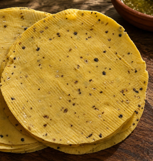 Yellow tortillas with black specks on a wooden surface